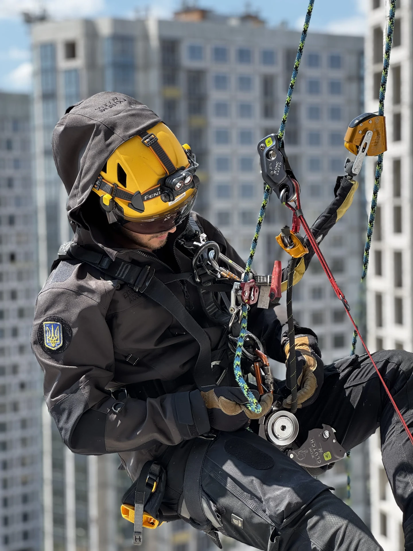 Rope access technician in Extreme Access workwear suspended at height with city buildings behind