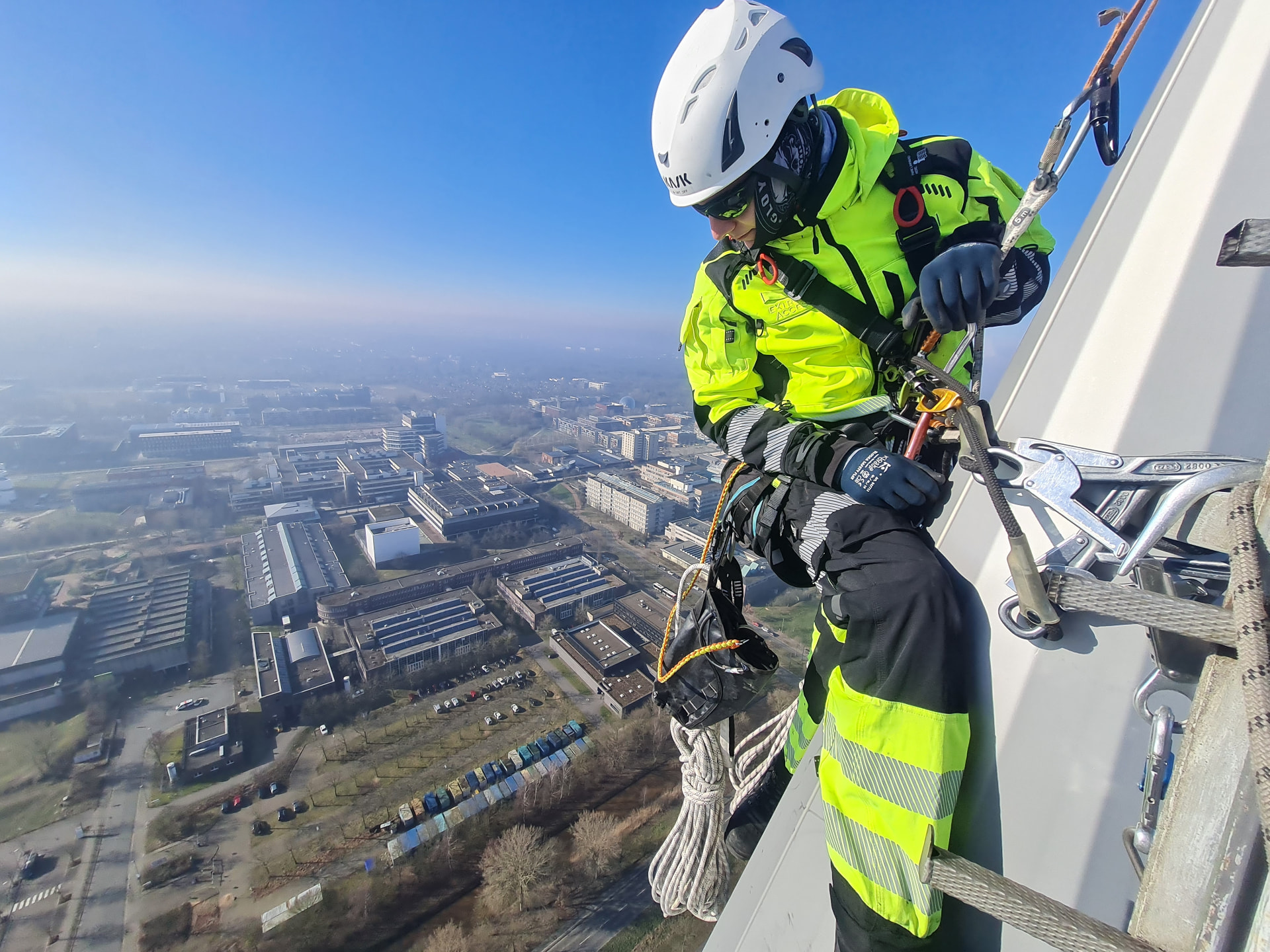 Technician wearing PERFORMANCE workwear in a harness beside a high-rise building