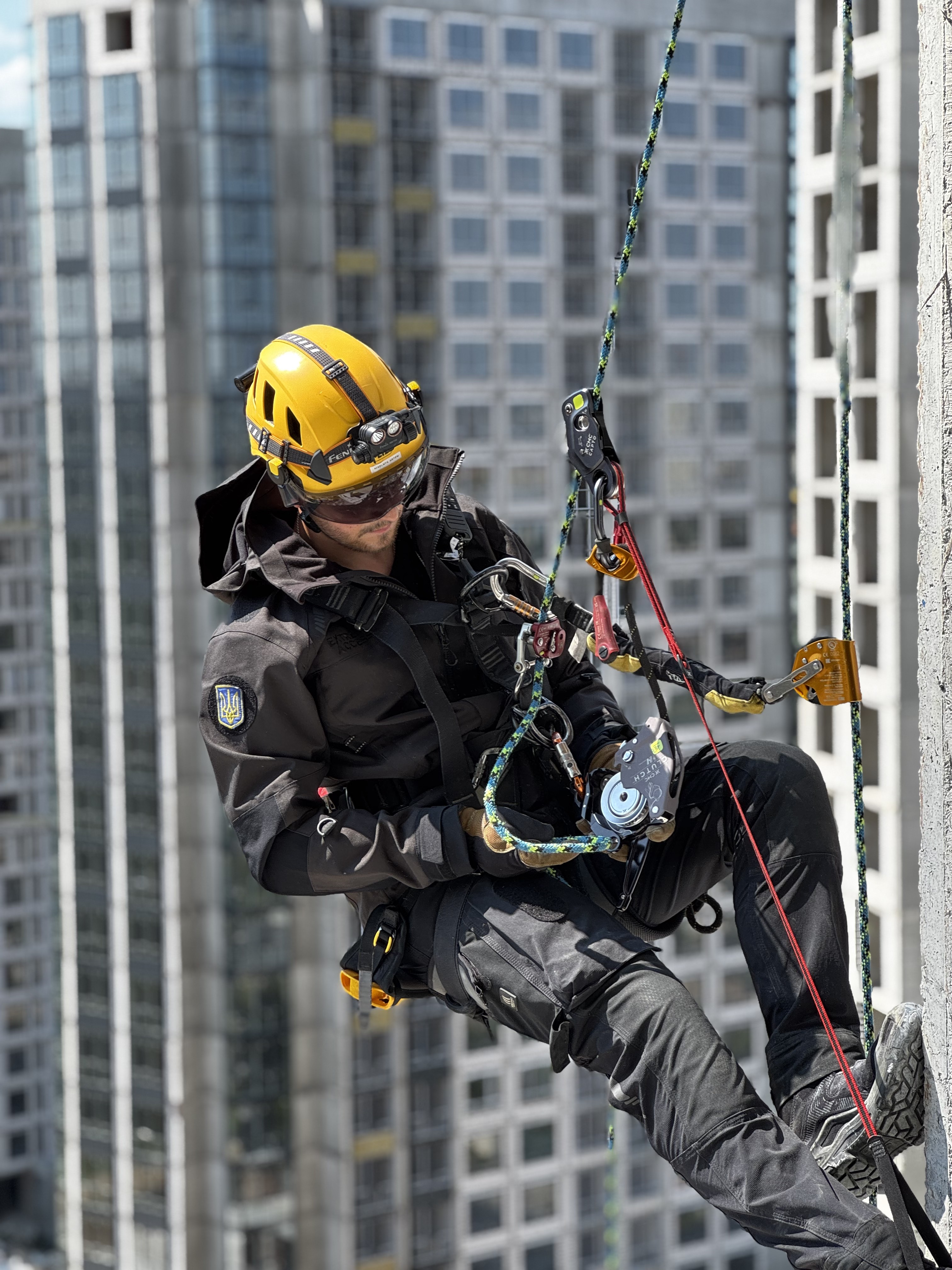 Rope access technician in DARK Extreme Access gear suspended on ropes beside city buildings