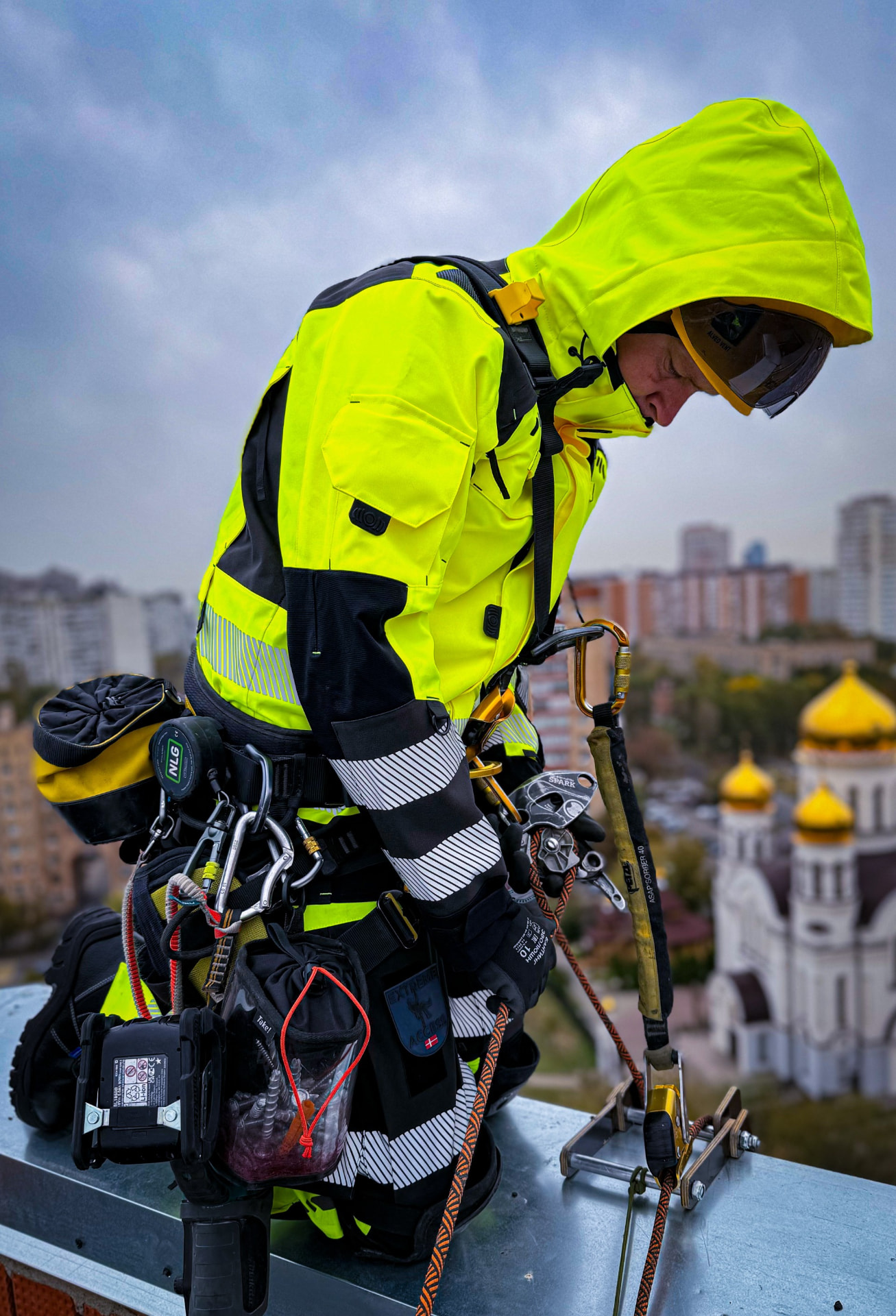 Rope access technician in a hi-vis Extreme Access jacket and harness working on a rooftop above a city